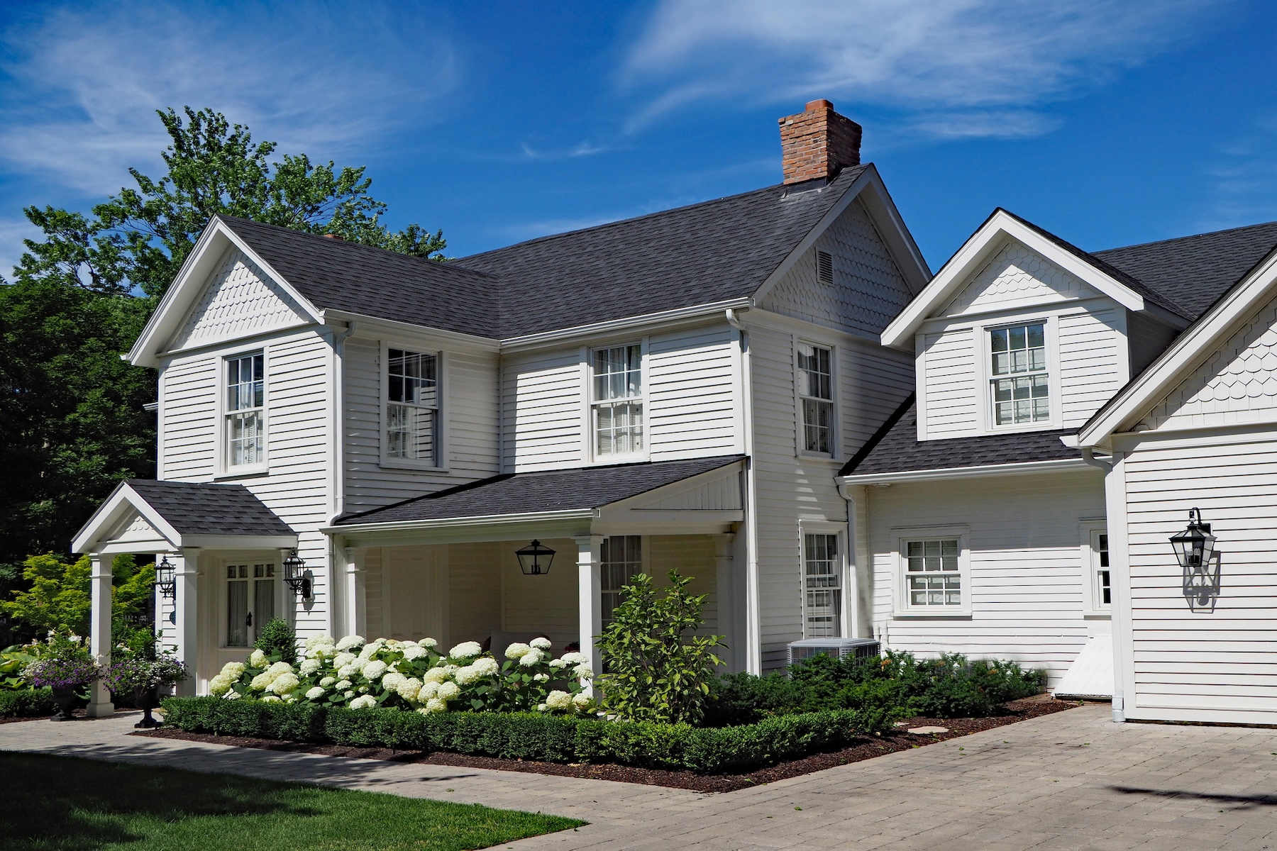 white house with dark roof. garden with white flowers in the front and a small covered porch